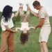 A joyful family enjoys outdoor play, lifting their child upside down in a green field.